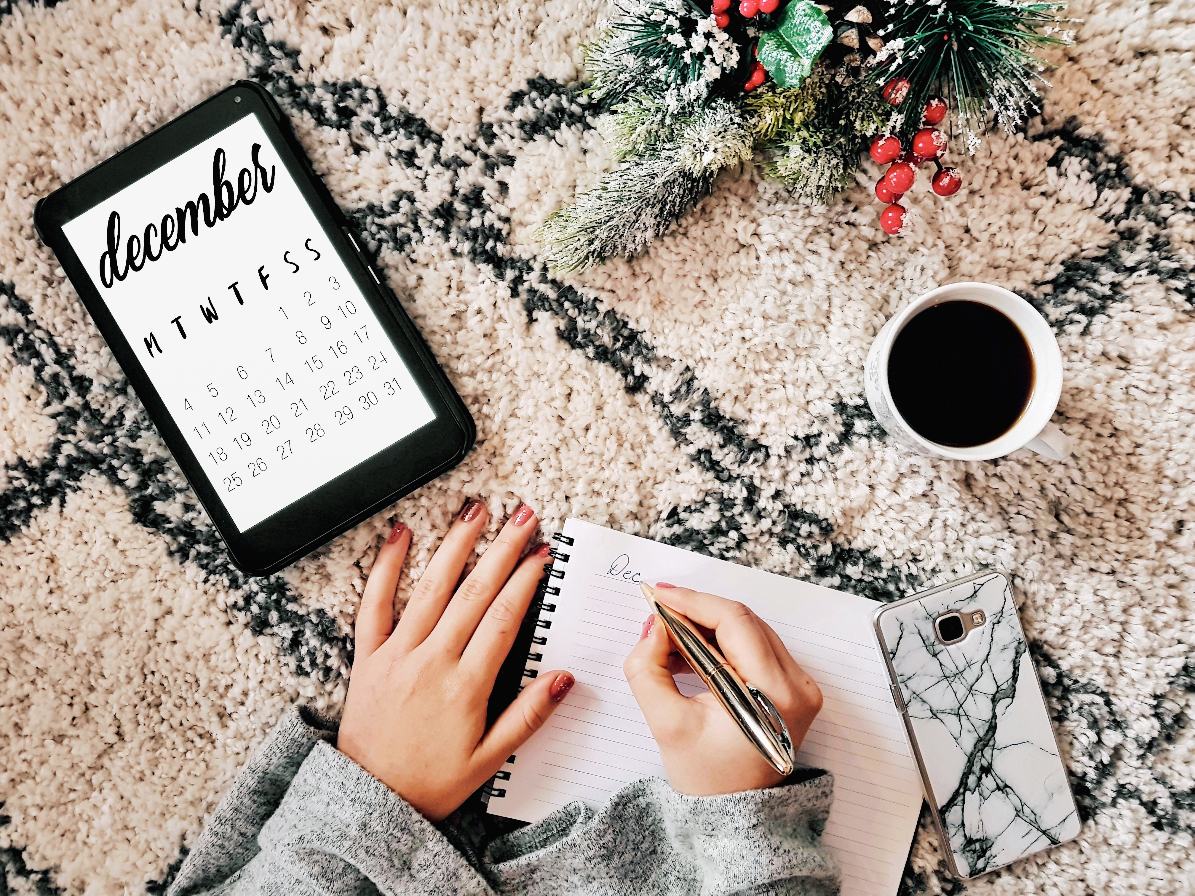 Christmas flat lay photo of woman writing in notepod next to cup of coffee and december calendar